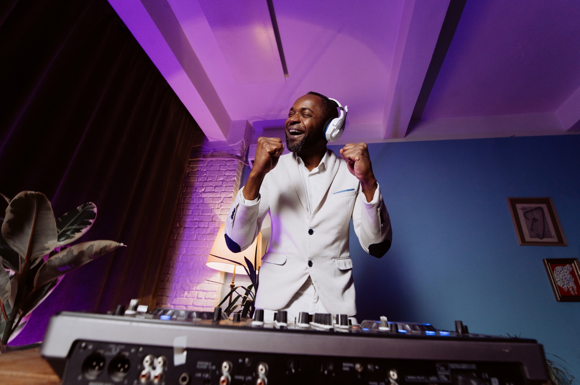 a DJ in a white suit listens to music, sings and dances. a man listens to music at a party.